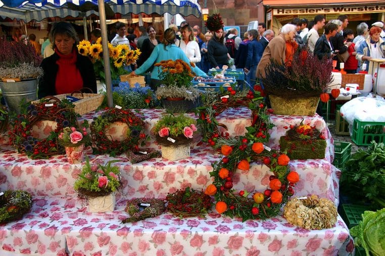 Étals de fleurs sur le marché de la Münsterplatz à Freiburg, prise horizontale, passants au second plan.