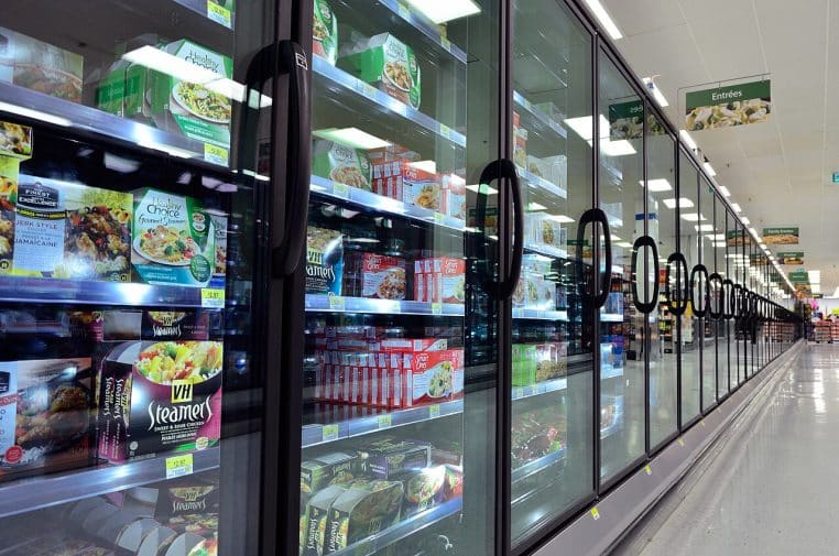 Grande allée de supermarché dédiée aux surgelés, avec bacs et vitrines alignés et signalétique suspendue.