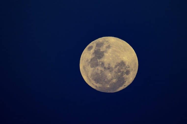 Disque lunaire jaune pâle sur un ciel bleu nuit uniforme, structure des cratères perceptible, prise de vue téléobjectif.