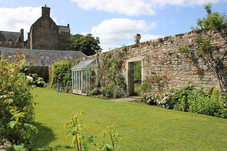 Jardinier entre haies et parterres verdoyants dans un jardin historique, occupé à l’entretien des massifs.