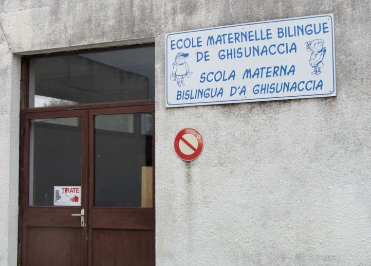 Entrée de l’école maternelle bilingue de Ghisonaccia avec panneau en français et en corse, illustrant l’enseignement en langue régionale sur l’île.