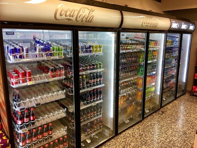 Rangée de vitrines réfrigérées à portes vitrées, éclairées, dans une allée froide de supermarché.