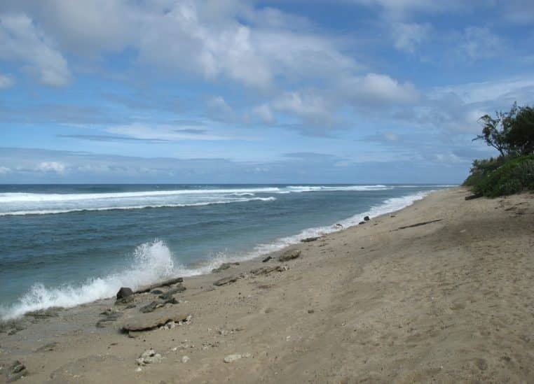 Plage et lagon de Grand Fond à Saint-Paul, avec sable clair au premier plan, eau peu profonde et houle qui vient se briser sur la barrière récifale.
