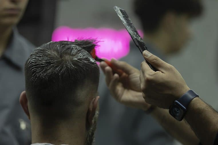 Coiffeur appliquant une coloration au pinceau sur les cheveux courts d’un client, vu de dos, dans un salon moderne légèrement flou