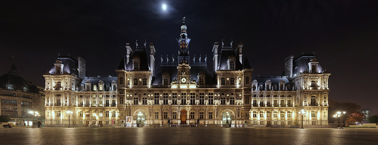 Vue large et détaillée de l’Hôtel de Ville de Paris de nuit, éclairé sur toute sa façade, illustrant le lieu central de l’administration municipale.