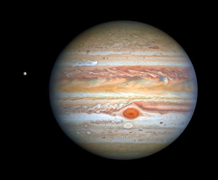 Vue du système jovien avec Jupiter en gros plan et la petite lune Europe éclairée, se détachant sur le fond noir de l’espace.