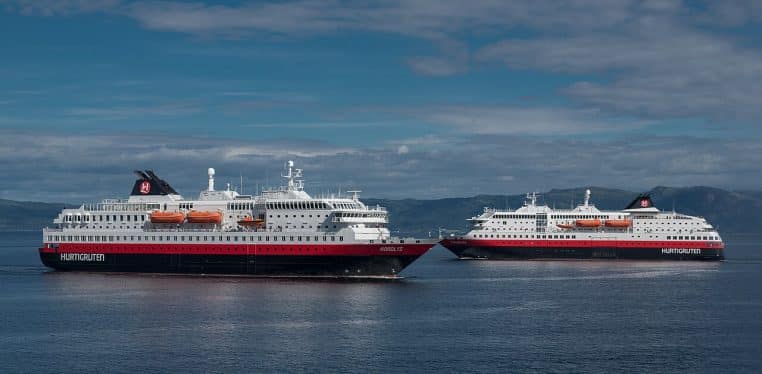 Deux navires de Hurtigruten naviguent dans un fjord norvégien sous un ciel clair, cadrage large et horizontal sur l’eau et les rives.