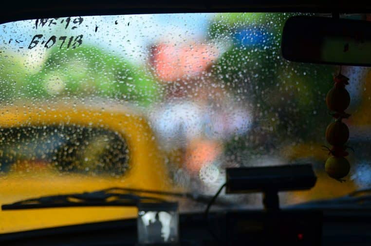 Habitacle de voiture vu depuis l’arrière, la route extérieure est visible au travers d’une vitre tachée de gouttes d’eau et de condensation.