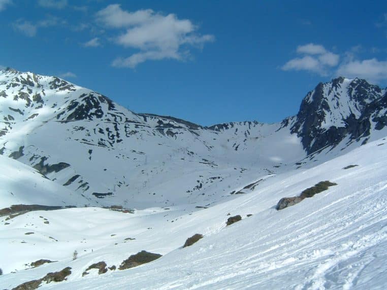 Vue enneigée du col du Tourmalet vers La Mongie, versants recouverts de neige sous un ciel bleu clair, reliefs bien marqués et traces sur le bas du champ.