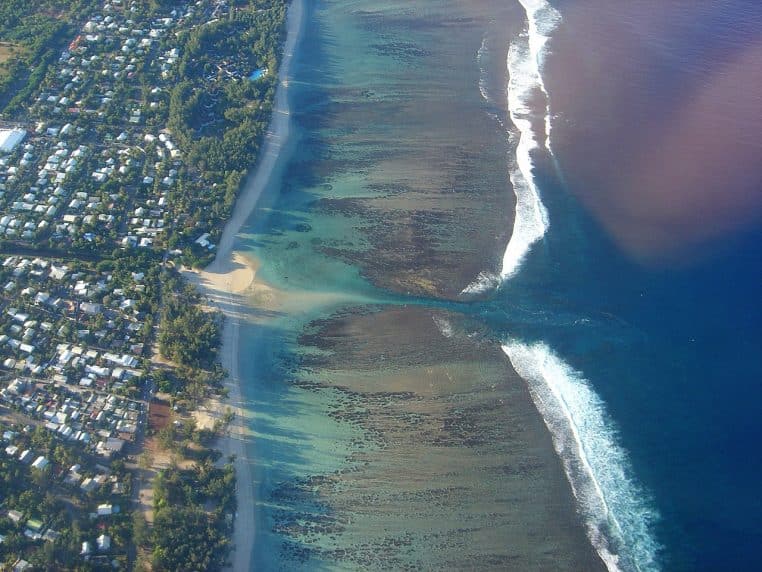 Vue aérienne du lagon de l’Hermitage à Saint-Paul, avec la barrière de corail, l’eau turquoise peu profonde et la plage bordée de végétation tropicale.