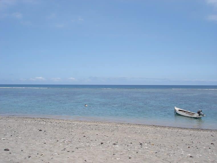 Panorama du lagon de la côte ouest de La Réunion par mer calme, montrant le récif frangeant, le ciel dégagé et la ligne de plage au second plan.
