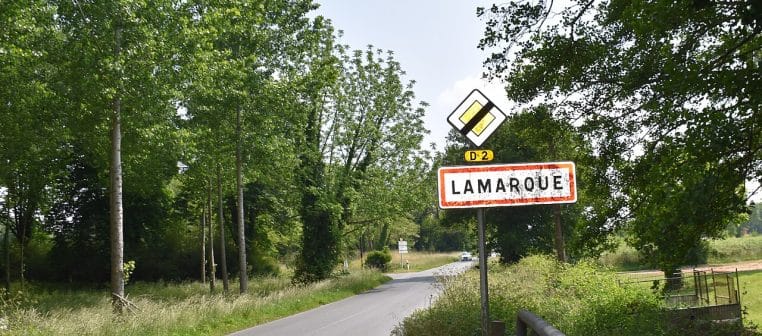 Panneau d’entrée de Lamarque en Gironde le long de la route, paysage horizontal avec végétation et ciel clair.