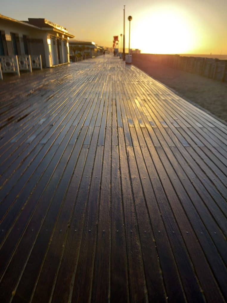 Promenade en bois des Planches à Deauville au coucher du soleil, reflets dorés sur les lattes face à la mer et au front de plage.