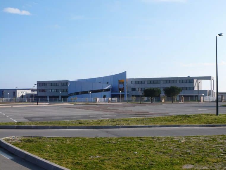 Vue d’ensemble du lycée de la plaine à Prunelli di Fiumorbu, bâtiment moderne entouré de parkings vides sous un ciel bleu lumineux.