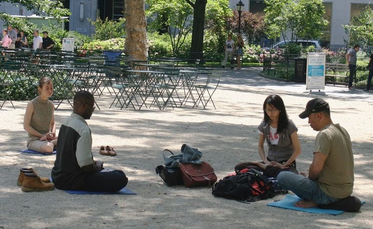 Personne assise en tailleur dans un parc new-yorkais, entourée de verdure, profitant d’un moment de calme et de solitude choisie