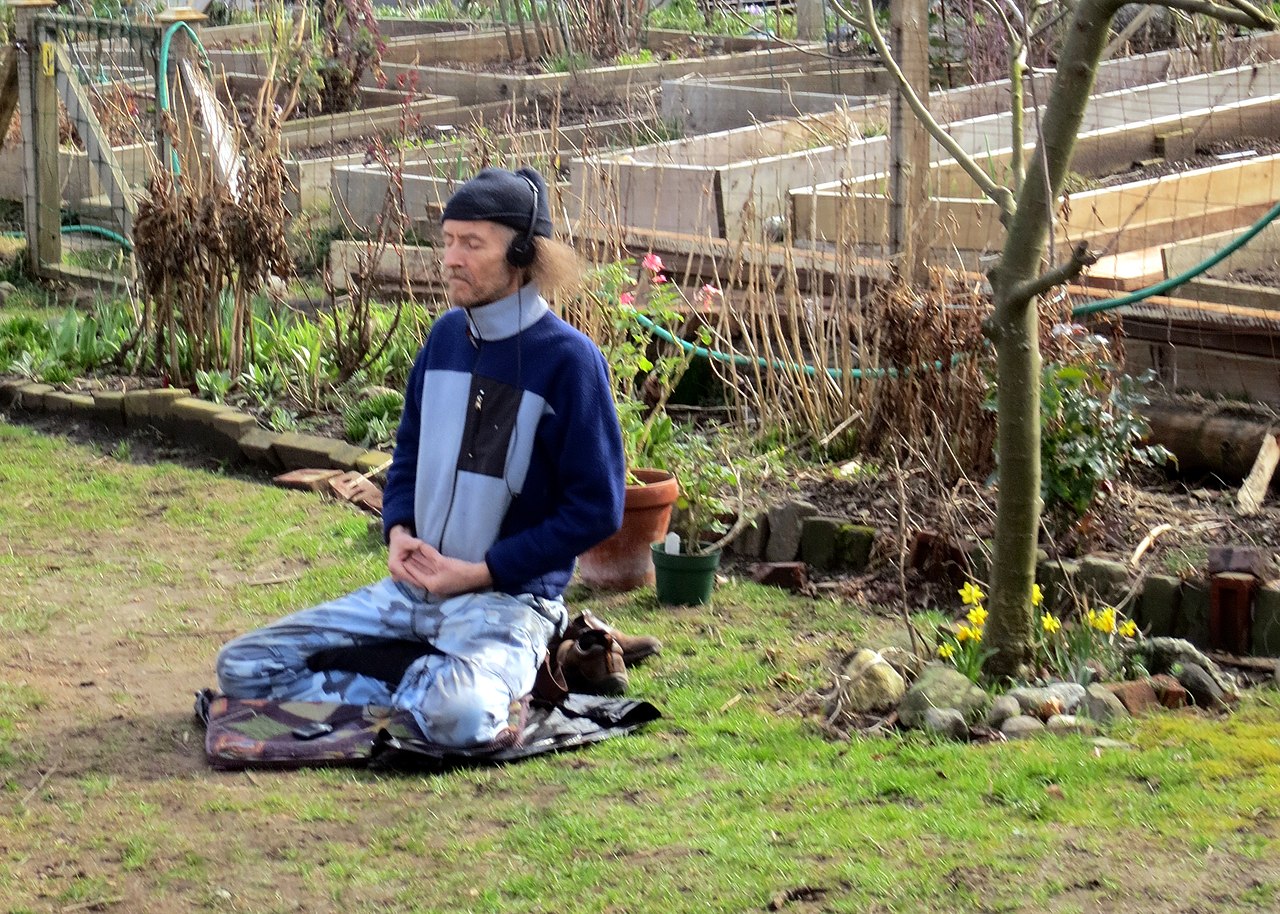 Personne méditant seule dans un jardin communautaire, entourée de plantes et de lumière douce en milieu de journée