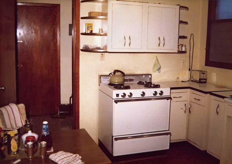 Cuisine de 1979 avec meubles intégrés, appareils rétro et étagères d’angle, ambiance chaleureuse et couleurs vintage.