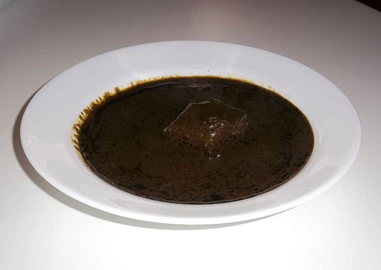 Assiette blanche contenant une mloukhya tunisienne sombre et onctueuse, avec un morceau de viande au centre.