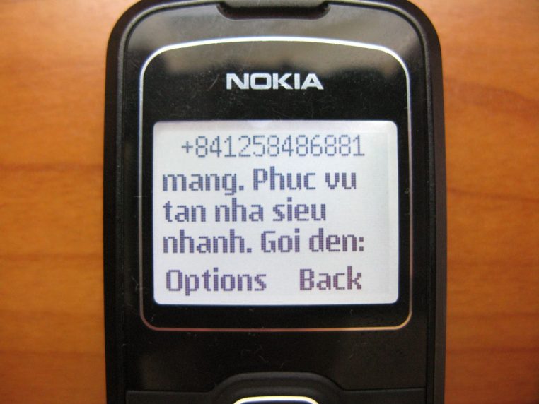 Téléphone mobile affichant un message de spam sur son écran, posé sur une table en bois, illustrant la prolifération des arnaques par SMS et appels.