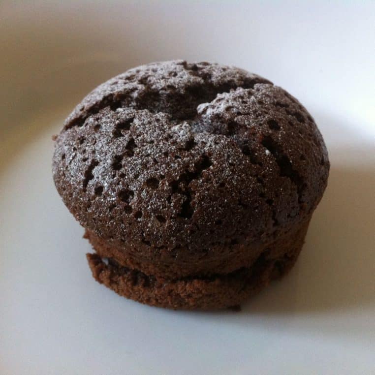 Moelleux au chocolat entier, croûte fine légèrement fendue, posé sur assiette blanche, éclairage chaud qui souligne le cœur fondant.