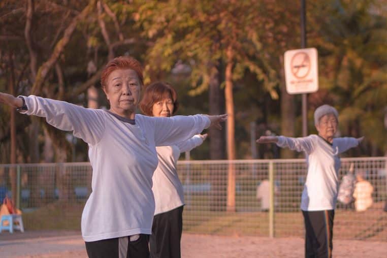 Groupe de seniors pratiquant le tai-chi dans un parc à Singapour, bras levés, mouvements synchronisés en matinée
