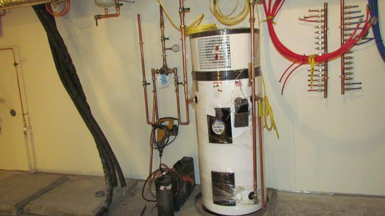 Chauffe-eau thermodynamique en cours d’installation, entouré de collecteurs et gaines, photo en intérieur d’un mur technique.