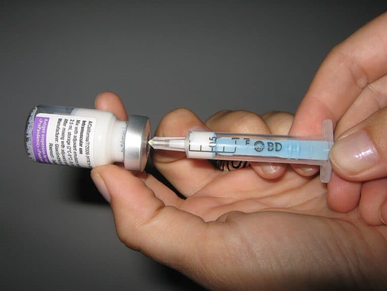 Mains d’un professionnel de santé tenant un flacon de vaccin Pandemrix et remplissant une seringue transparente en vue d’une injection.
