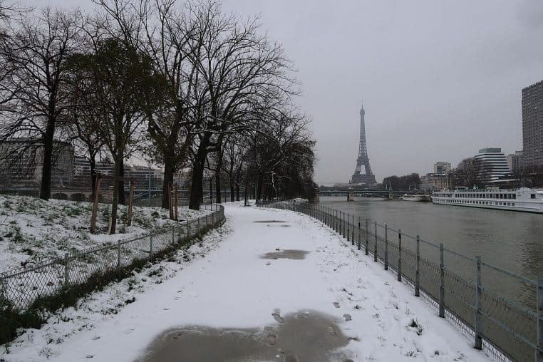 Chemin enneigé le long de la Seine sur l’Île aux Cygnes à Paris, arbres dénudés et tour Eiffel qui se détache dans la brume hivernale.