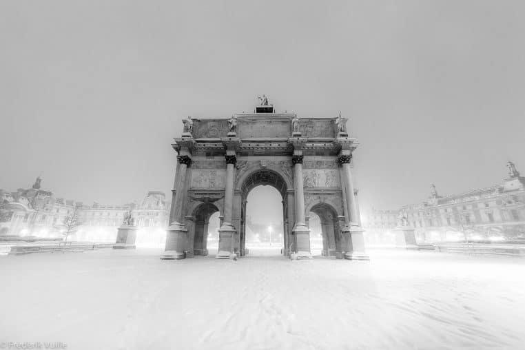 Arc du Carrousel du Louvre entouré de neige fraîche, dans une perspective large sur le palais et la cour silencieuse.