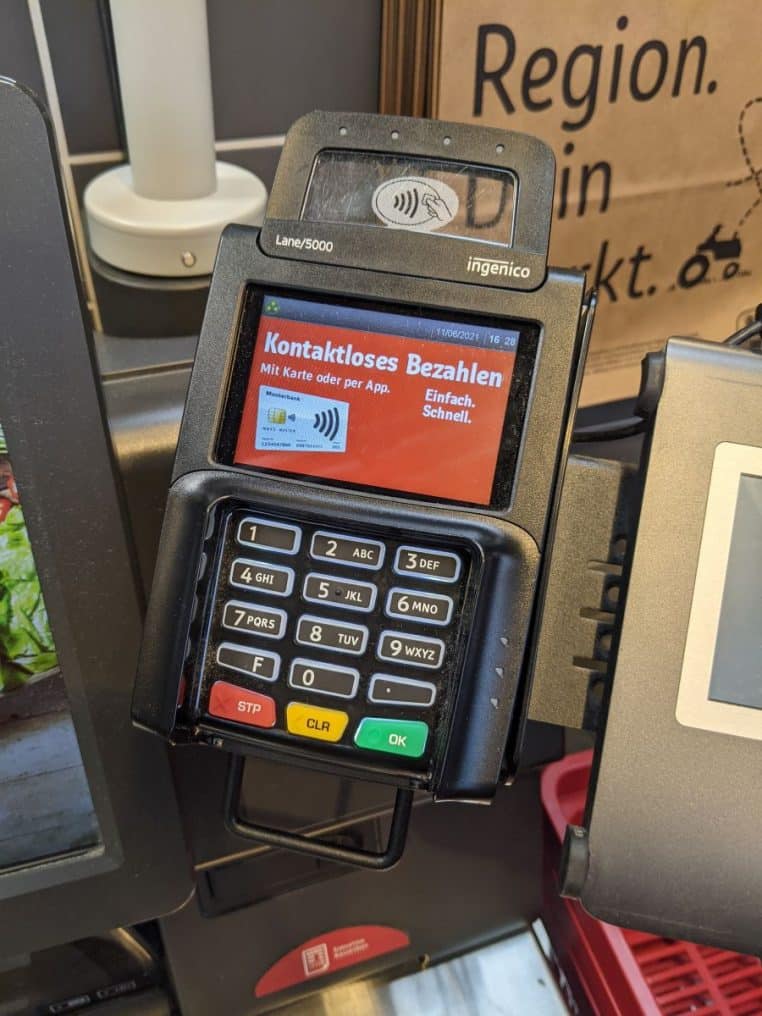 Terminal de paiement installé sur une caisse automatique de supermarché, écran allumé prêt à enregistrer un achat en libre-service.