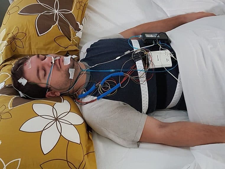 Sujet relié à des capteurs de polysomnographie en clinique du sommeil, capteurs EEG et thoraciques visibles sur le torse.