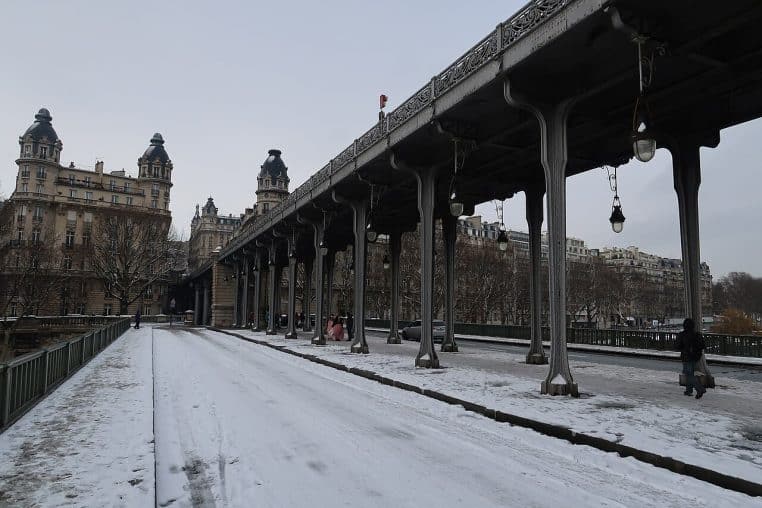 Pont de Bir-Hakeim à Paris recouvert d’une fine couche de neige, chaussée glissante et immeubles haussmanniens sous un ciel uniformément gris.