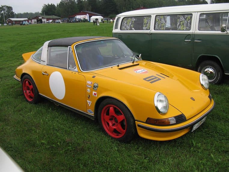 Porsche 911 Targa classique photographiée de profil sur un parking, avec sa ligne emblématique bien visible et son toit partiellement ouvert.
