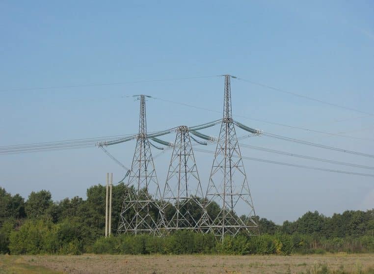 Alignement de pylônes électriques à haute tension traversant un paysage rural, ciel dégagé et perspective fuyante.