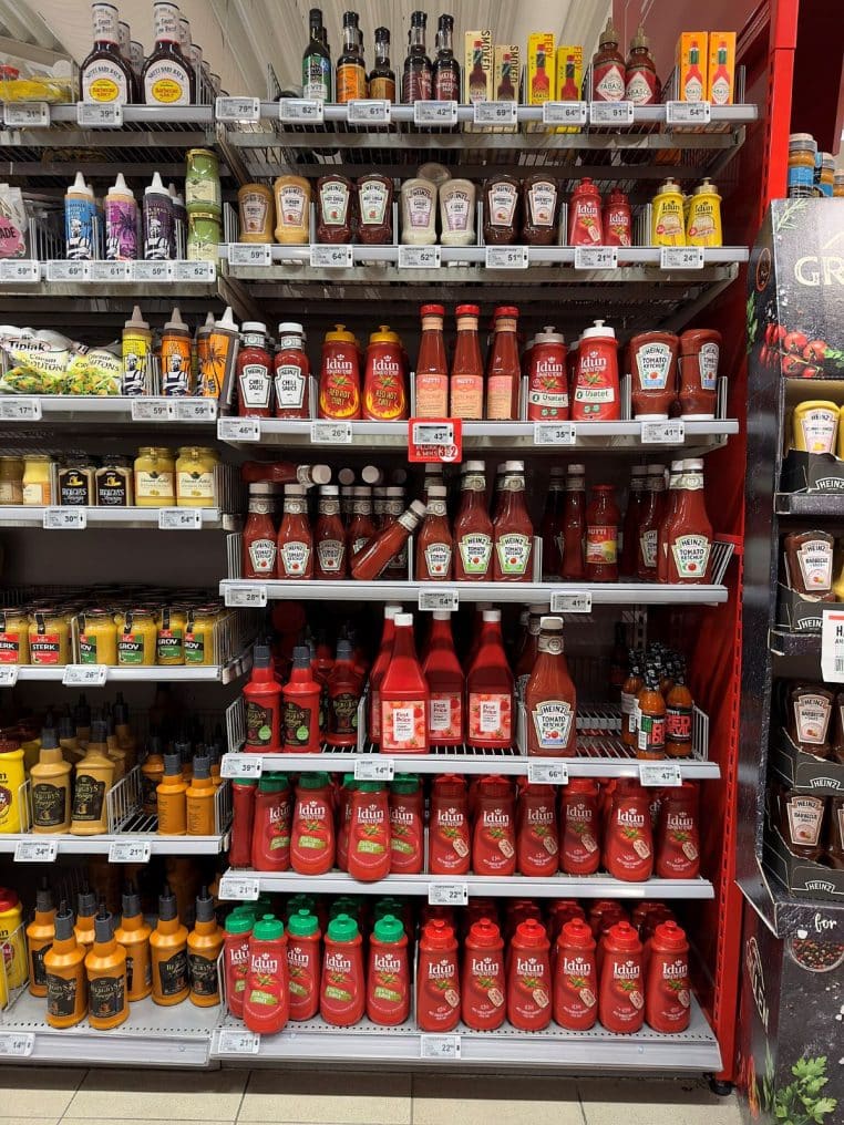 Rayon de condiments en supermarché avec ketchups et sauces, vue d’ensemble horizontale des étagères dédiées aux sauces.