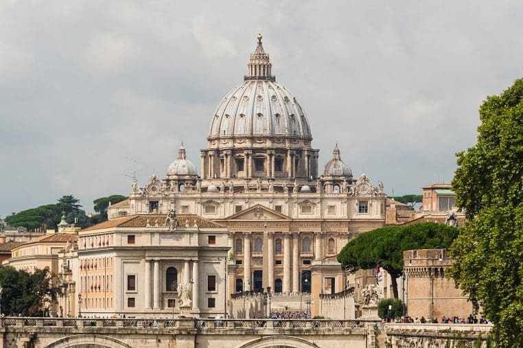 Façade de la basilique Saint-Pierre au Vatican, colonnades et statues apostoliques sous un ciel lumineux.