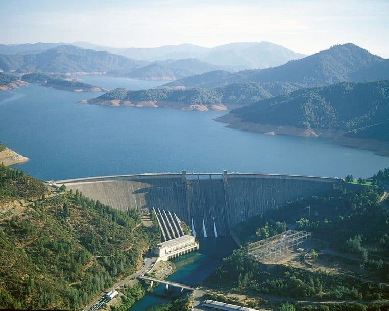 Vue générale du barrage de Shasta retenant un lac de retenue bleu, avec les structures en béton dominantes au centre.