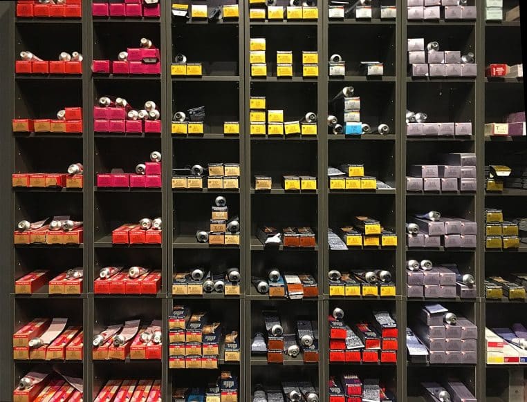 Grande étagère de salon remplie de boîtes de colorations professionnelles multicolores soigneusement rangées par colonnes et références