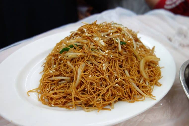 Assiette de nouilles sautées dorées à la sauce soja, avec légumes croquants, rappelant une poêlée rapide inspirée de la street-food asiatique.v