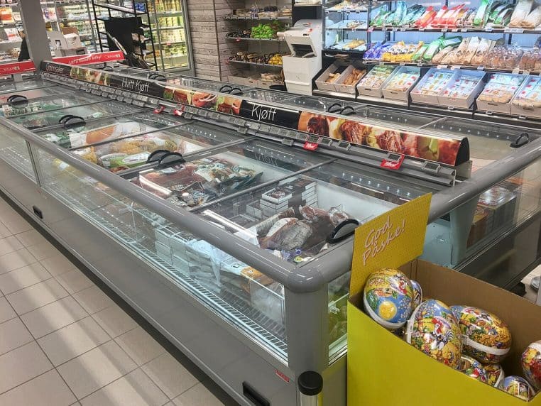 Congélateurs coffres à couvercles vitrés alignés dans un supermarché, dédiés aux produits surgelés comme viandes et pizzas.