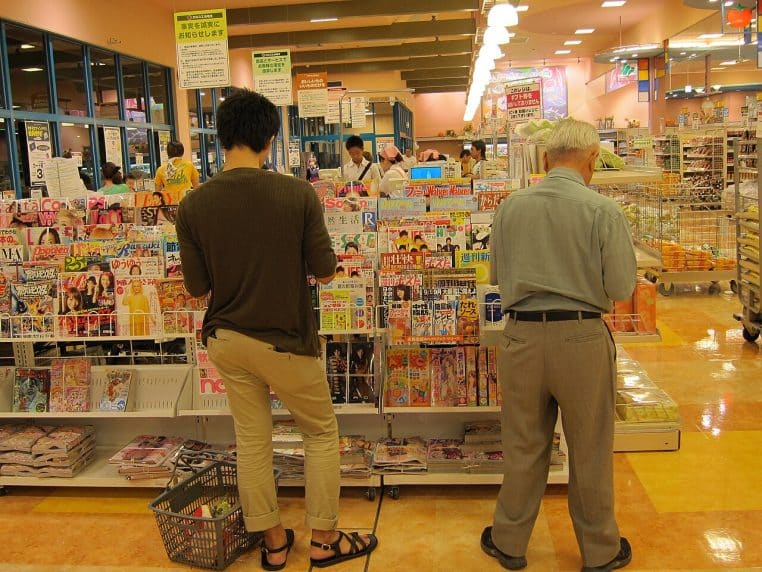 Vue d’ensemble d’un supermarché avec des clients consultant les magazines près de la sortie et les caisses au second plan.