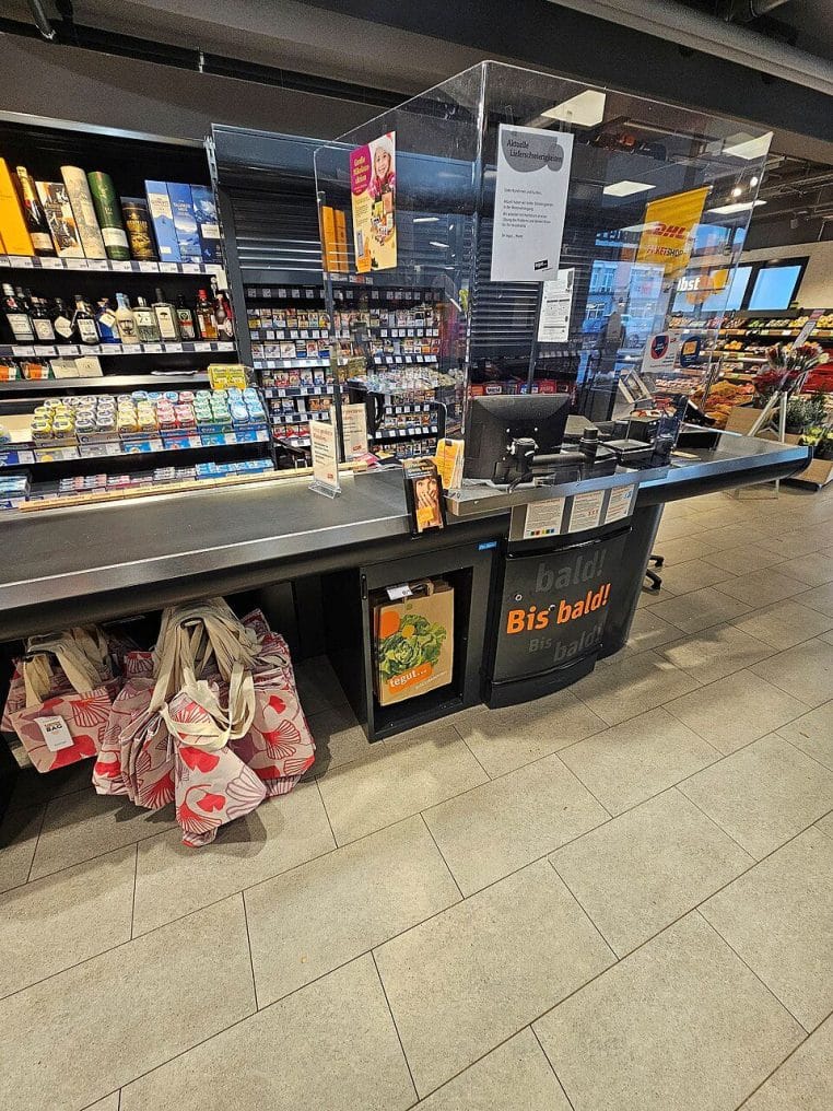 Poste de caisse moderne avec tapis roulant, protections transparentes et sacs réutilisables empilés au bout du comptoir.