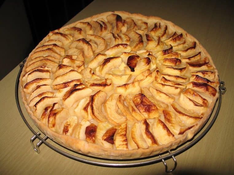 Tarte aux pommes familiale disposée en spirale, bords dorés et surface caramélisée, posée sur une grille de refroidissement.