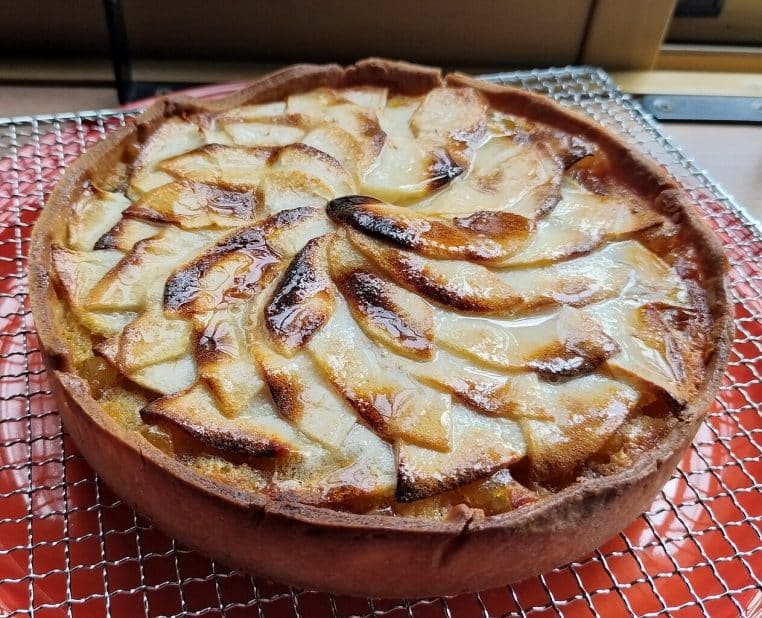 Tarte aux pommes brillante sortant du four, lamelles bien dorées et bordure épaisse, reposant sur une grille.