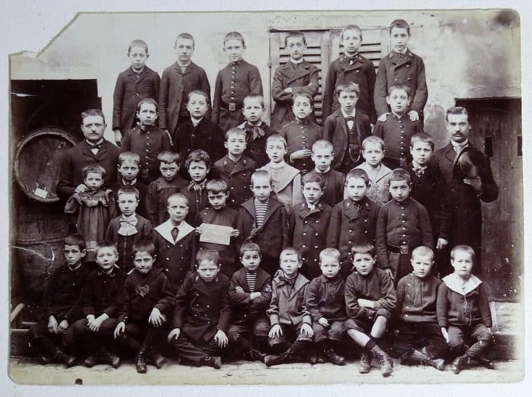 Ancienne photo de classe à Taverny vers 1880 : rangées d’élèves posant avec leur instituteur devant l’école.