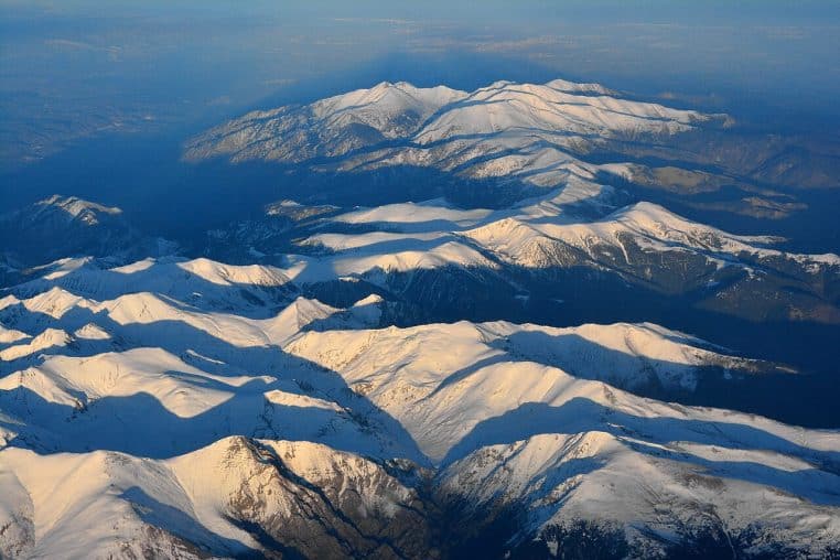 Chaîne des Pyrénées photographiée depuis les airs au crépuscule, crêtes enneigées et vallées sombres.