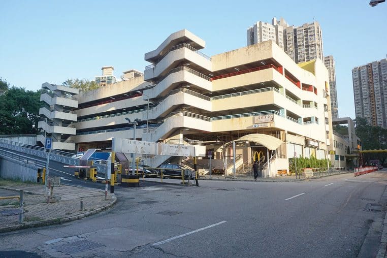 Parking aérien d’un centre commercial de quartier avec rampes, barrières d’accès et plusieurs voitures en déplacement.