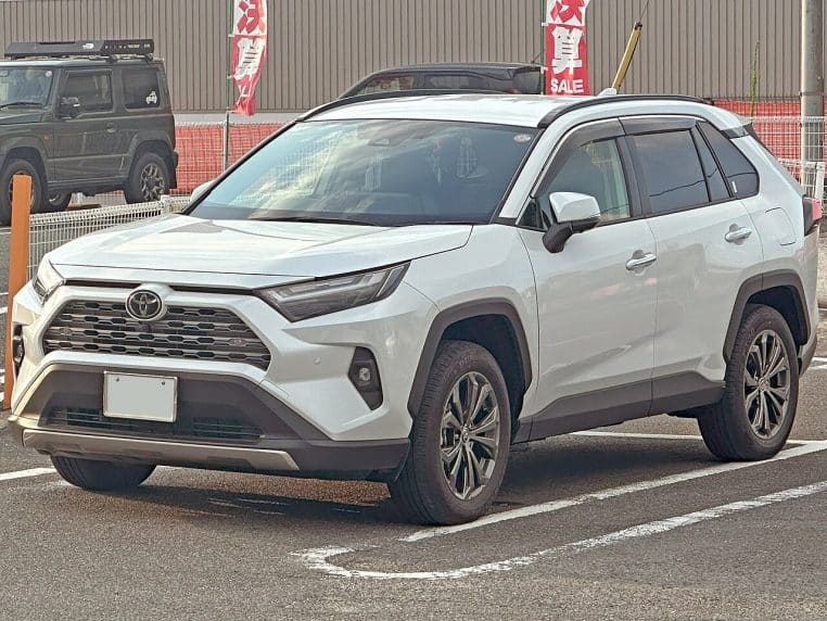Toyota RAV4 hybride blanc stationné sur un parking, photographié en trois-quarts avant, montrant clairement sa silhouette de SUV familial.
