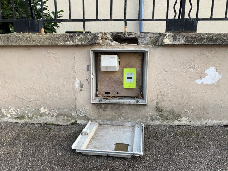 Coffret mural ouvert avec compteur Linky vert intégré dans un muret de rue à Lyon, vue frontale en extérieur en pleine journée.