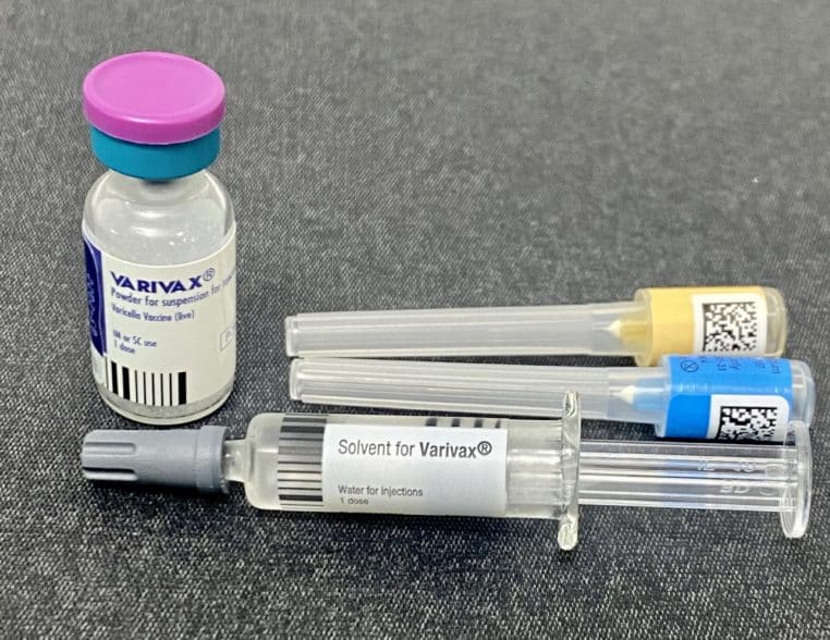 Flacon de vaccin VARIVAX posé sur une surface grise avec trois seringues préremplies alignées à côté, prêtes pour une séance de vaccination.